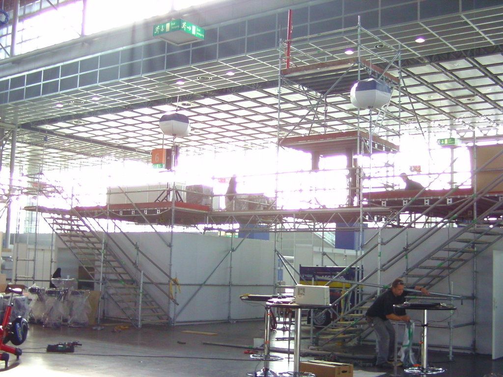 Raumgerüst in einer Messehalle mit Arbeitsebene unter der Hallendecke und Aufgängen an beiden Seiten
